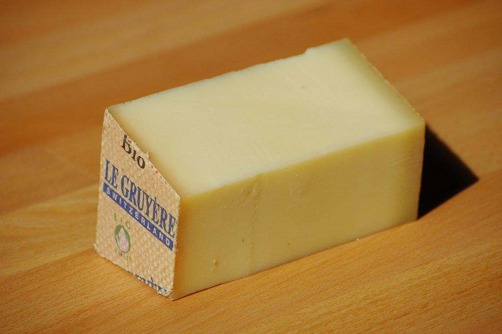 A wedge of Gruyère cheese beside a grater