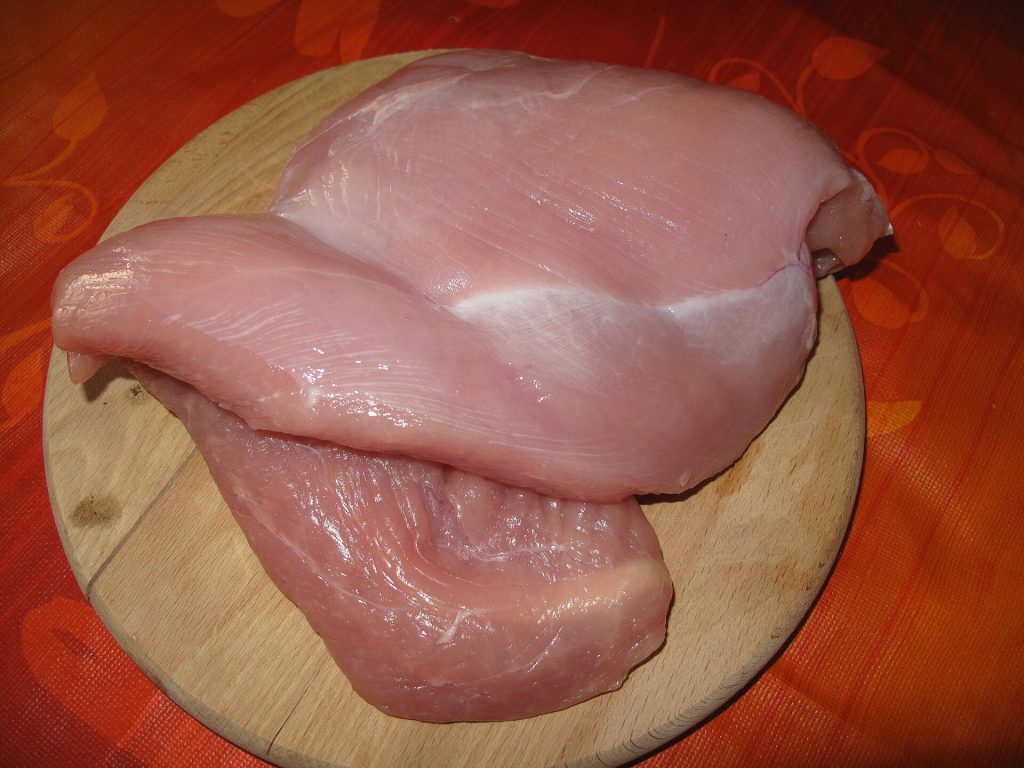 A wrapped whole turkey thawing on a refrigerator shelf