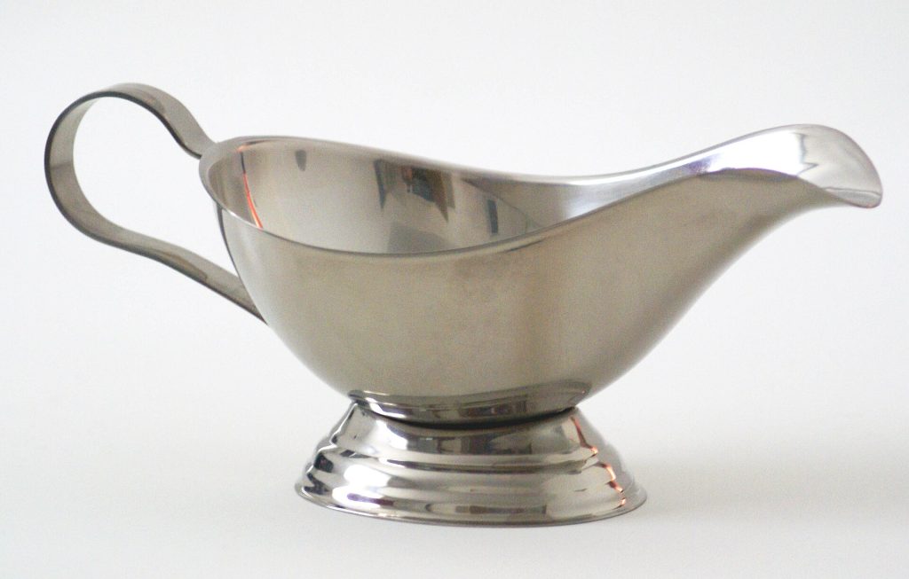 Gravy in a serving boat next to a roasting pan
