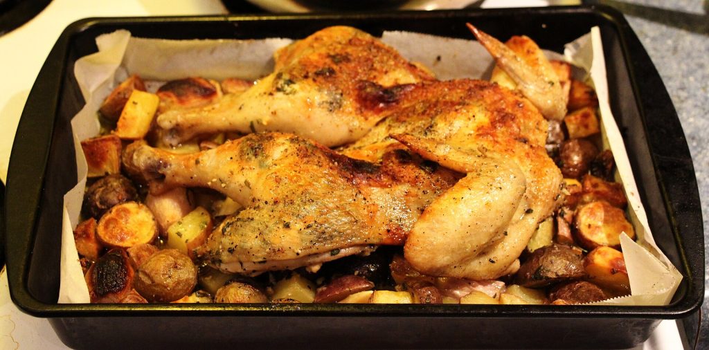 A roast chicken and potatoes in a deep roasting pan
